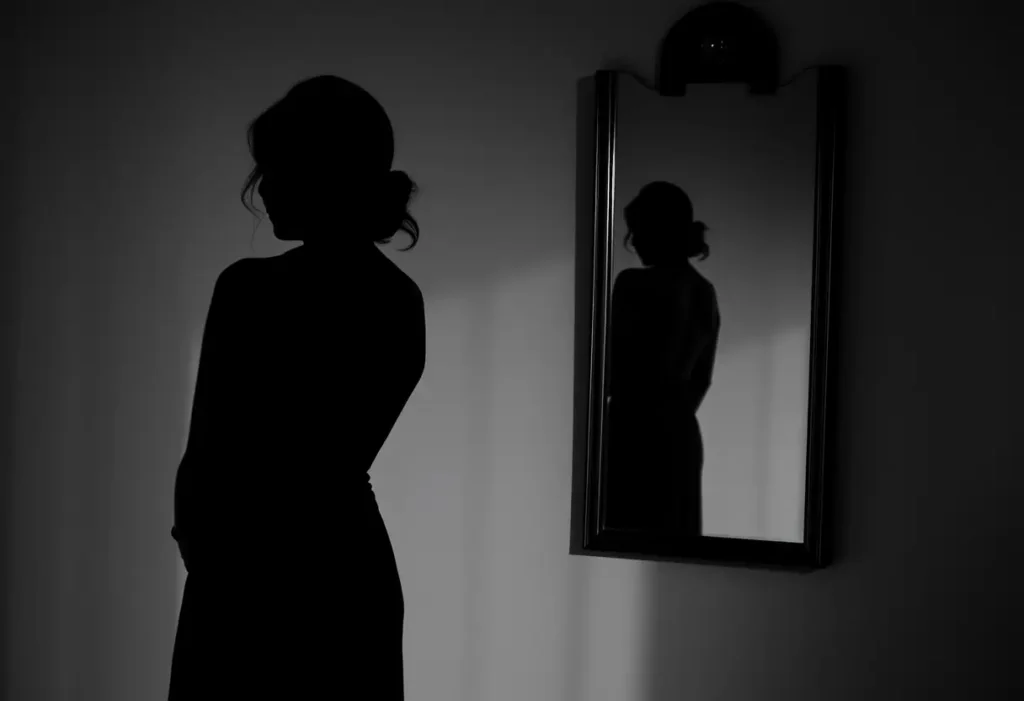 Silhouette de femme se reflétant dans miroir mural, arborant une robe sans manches gracieusement drapée.