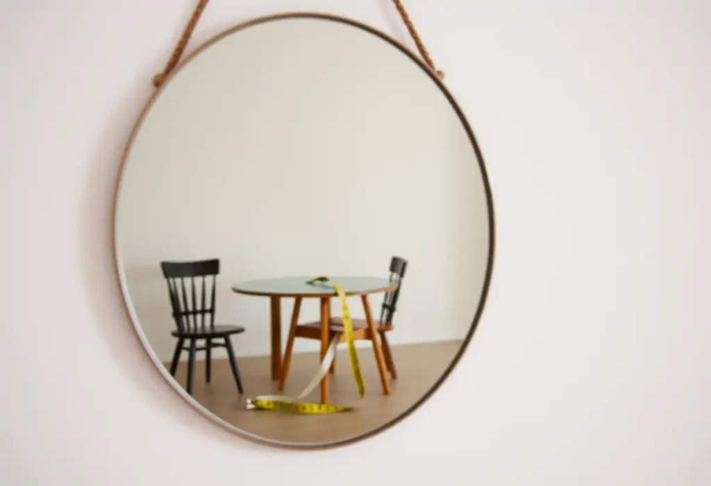 Miroir simple reflétant une pièce avec une table et un tabouret où repose un mètre ruban