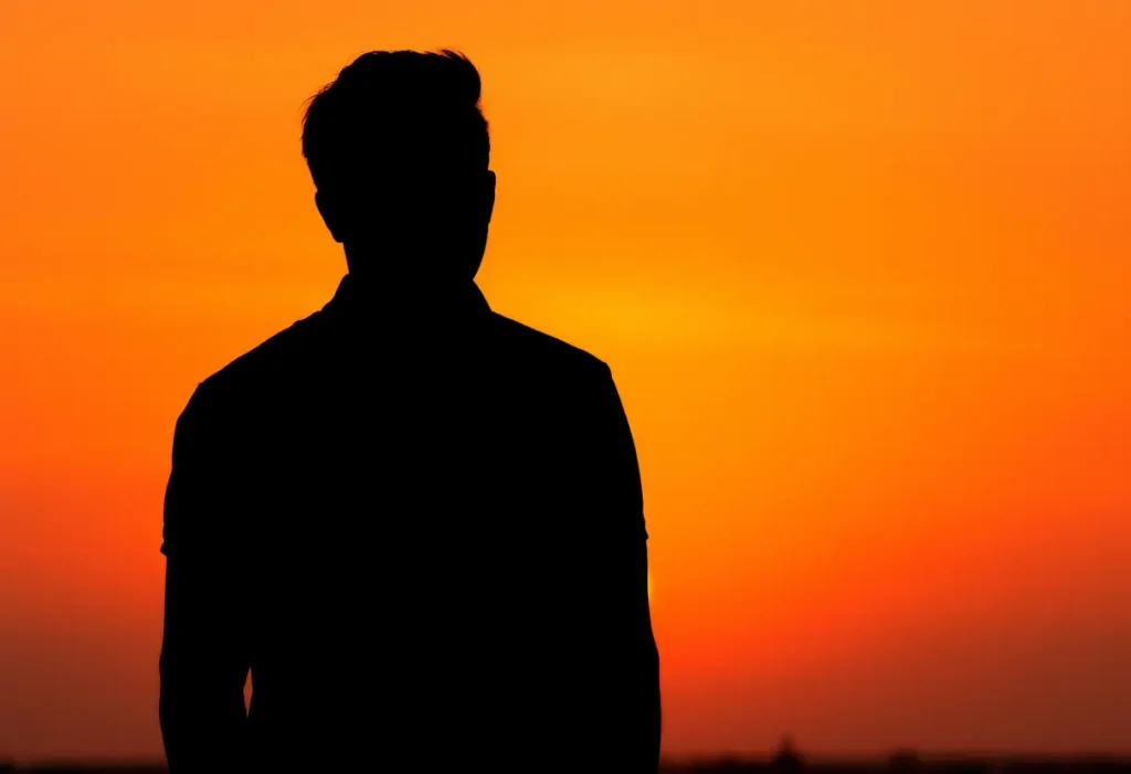 Un profil silhouetté devant un coucher de soleil orangé, pensif sur les souvenirs et rêves communs